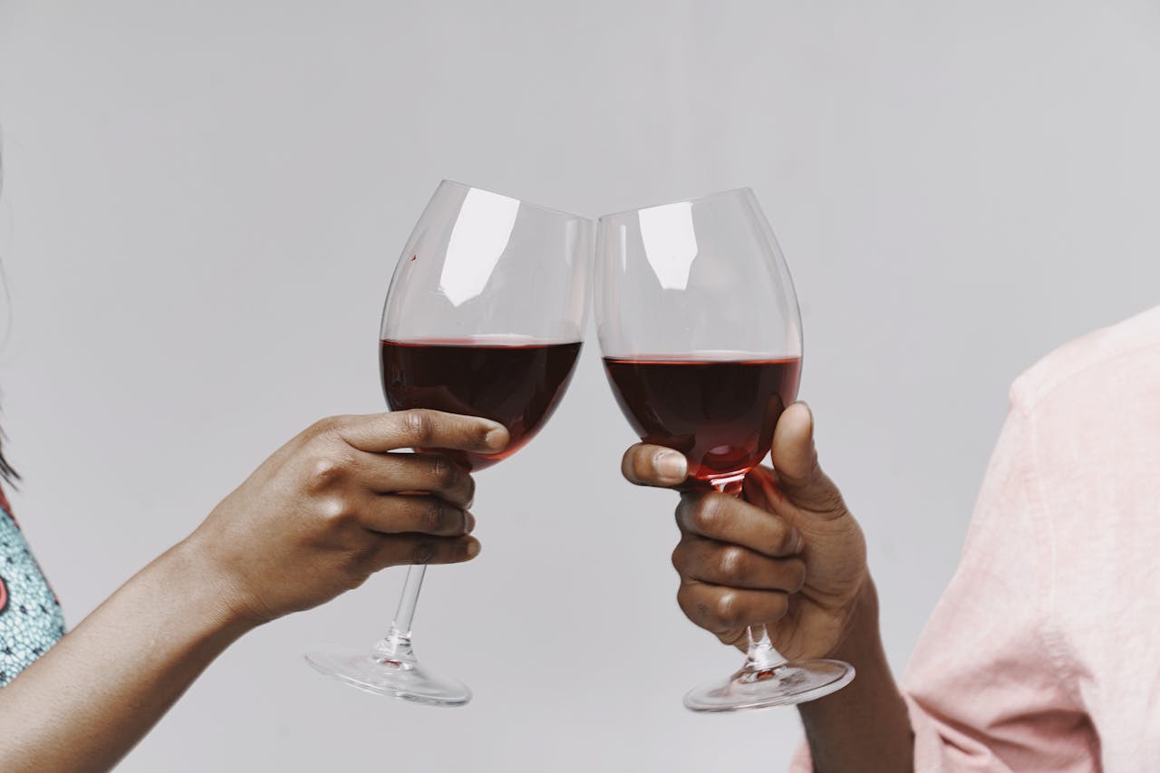 about-us Two people toasting with red wine glasses on a clean white background, evoking celebration and togetherness.
